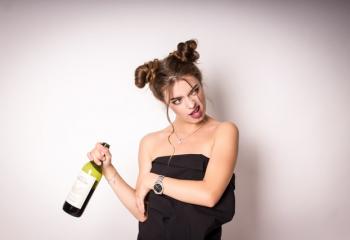Photo of a woman holding an open bottle of wine with a questioning look on her face