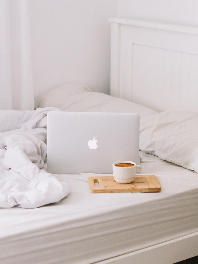 Laptop and coffee on an unmade bed